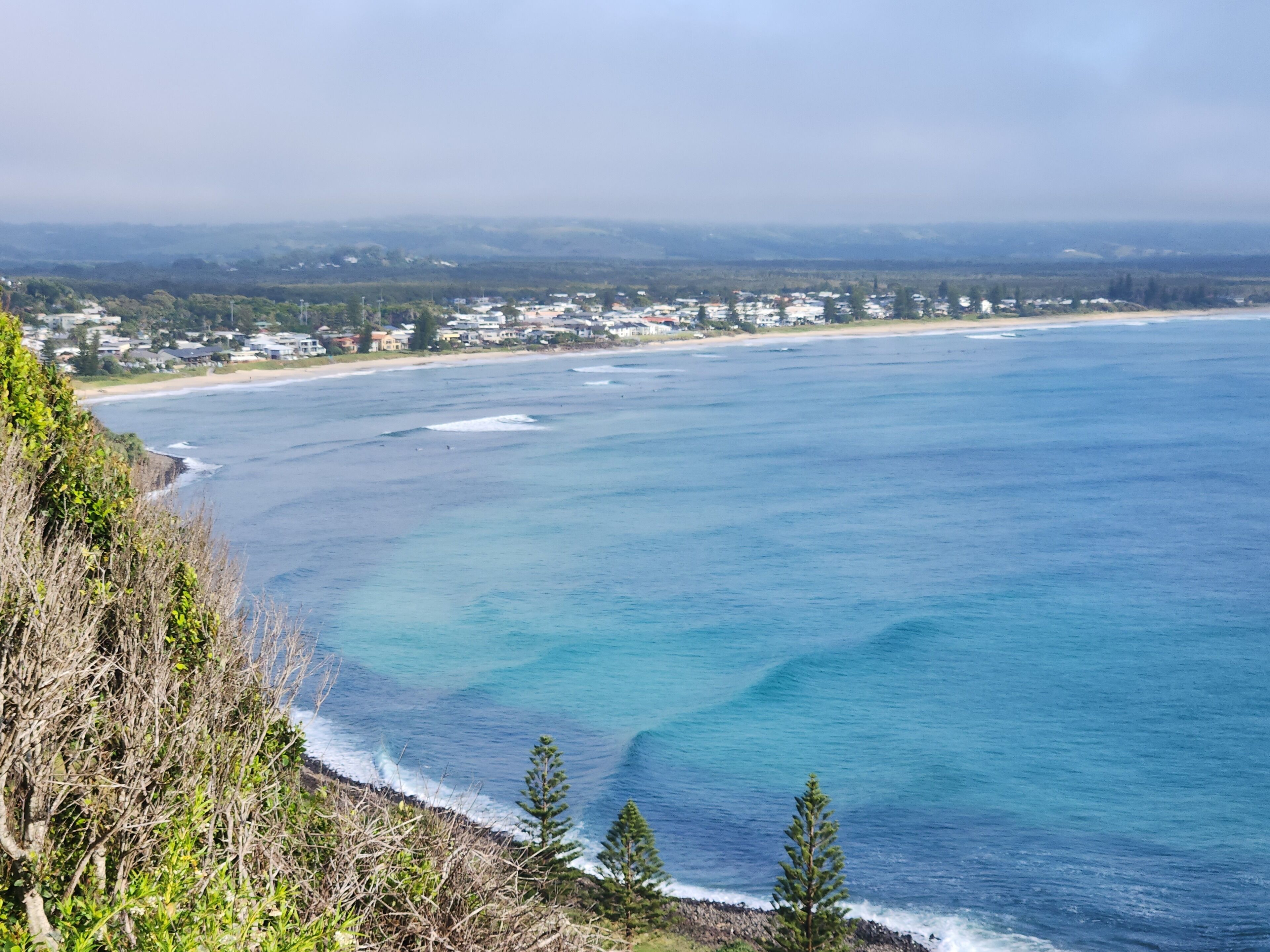 A coastal view with a beach, ocean, and a town in the background.