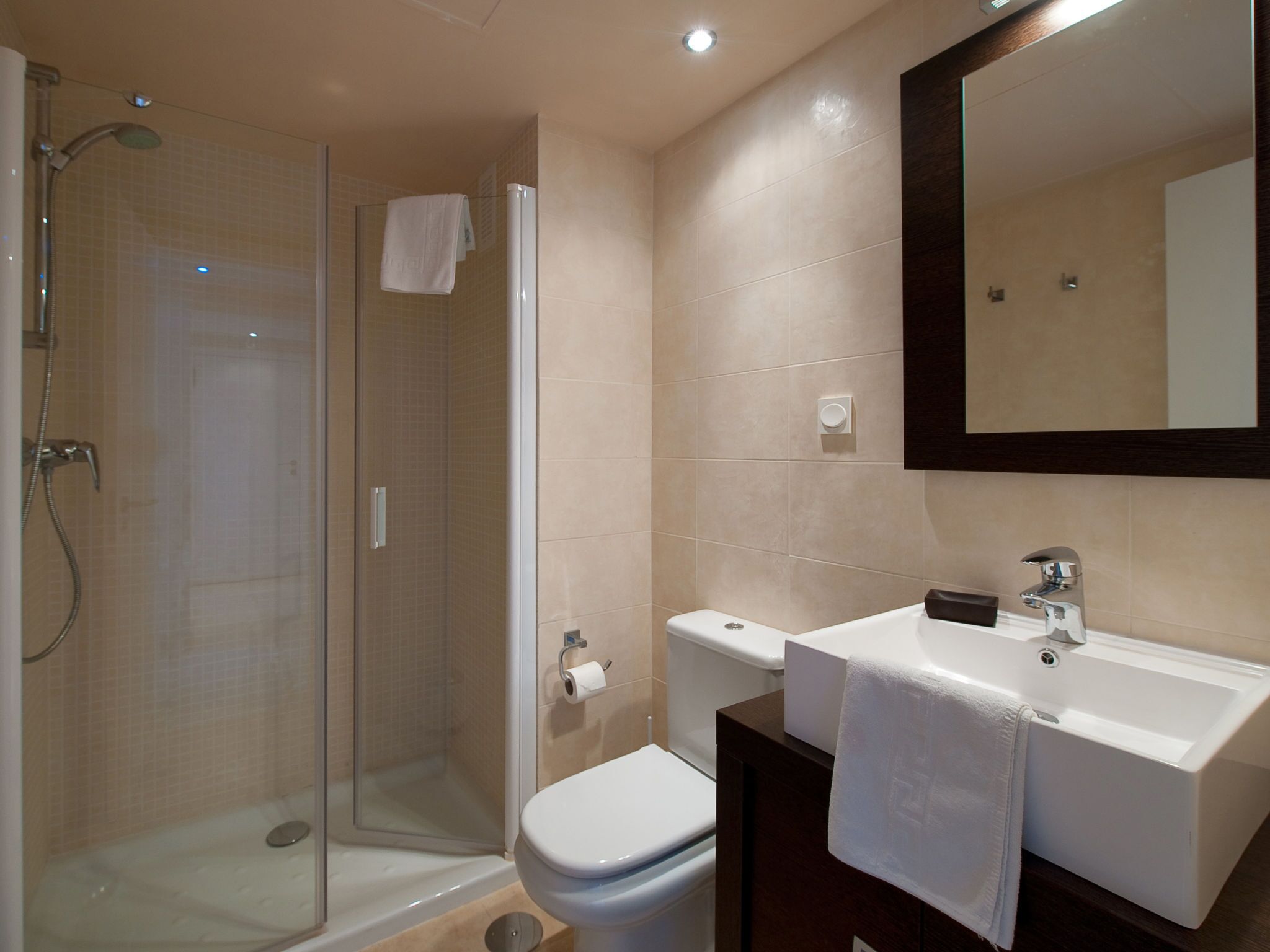 Un baño moderno con ducha de vidrio, inodoro blanco, lavamanos con espejo y una toalla colgada en la pared.