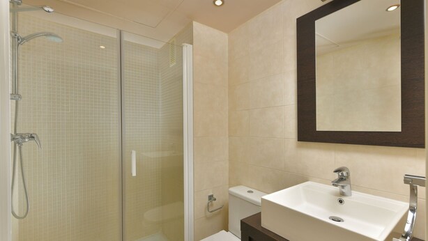 Une salle de bain moderne dotée d’une douche à parois de verre, de toilettes blanches et d’un grand lavabo avec un meuble-vasque en bois foncé.