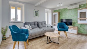 Una sala de estar moderna con un sofá gris, dos sillones azules, una mesa de centro de madera, un televisor de pantalla plana y una pared de acento verde.
