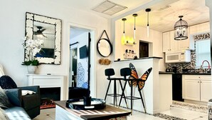 Eine moderne Küche mit weißen Schränken, einer Mikrowelle und einer Chandelieber. Es gibt einen Essbereich mit Tisch und Stühlen sowie ein Wohnzimmer mit Sofa und Kamin.