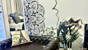 Ein Wohnzimmer mit einem schwarzen Ledersofa, einem dekorativen Kissen mit dem Eiffelturm, einer großen schwarz-weißen Blütenleiste an der Wand und einem einzigartigen sternförmigen Spiegel.