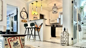 Eine moderne Küche mit weißen Schränken, einer schwarzen Arbeitsplatte und einem Teppich mit ZEBRA-Muster. Zwei schwarze Stühle mit Schmetterlingsmotiven, eine Pendelleuchte und ein dekorativer Laterne sind vorhanden.
