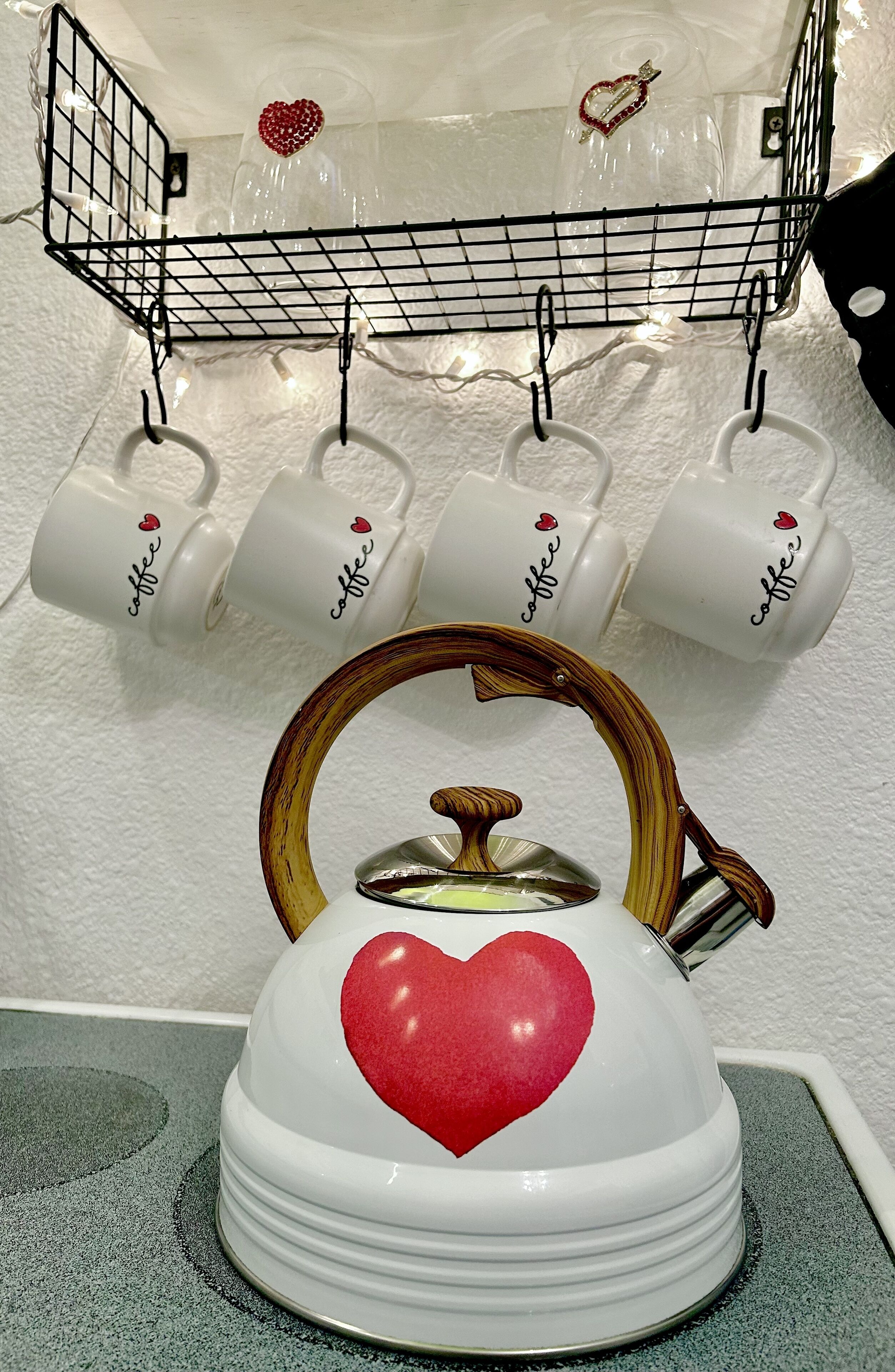 Una tetera blanca con asa de madera y un diseño de corazón rojo, sobre una encimera de cocina.