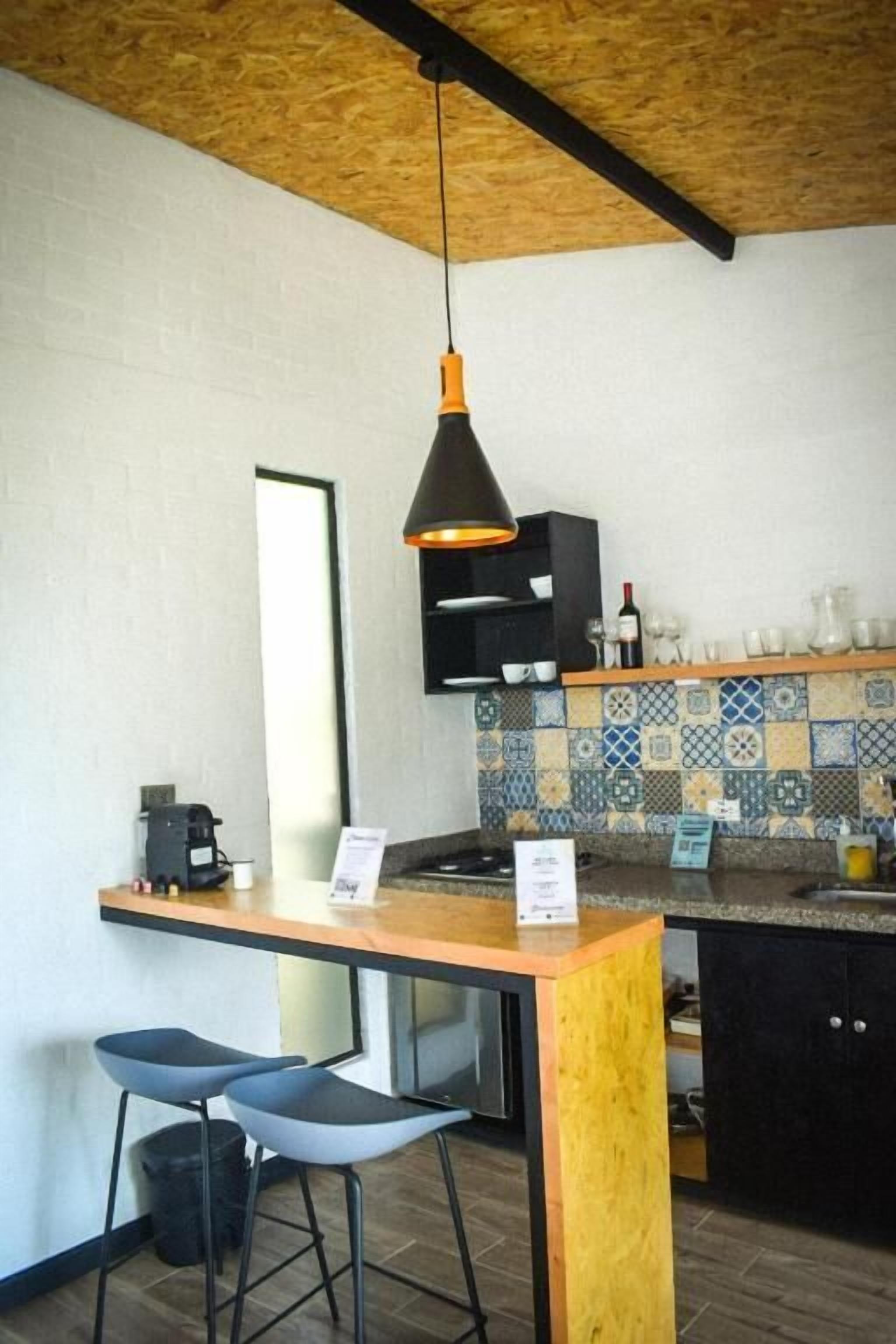 Een keuken met een houten plafond, een hangende hanglamp, een koffieapparaat en een betegelde achterwand.