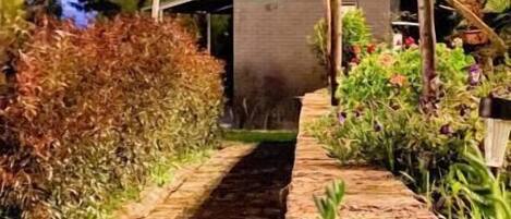 A pathway lined with greenery and a brick wall, leading to a building with a visible entrance.