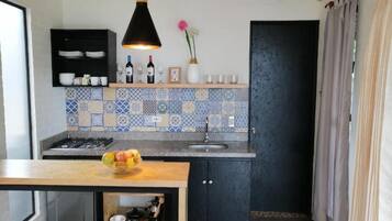 A compact kitchen with a tiled backsplash, a wooden countertop, and a black hanging light fixture.