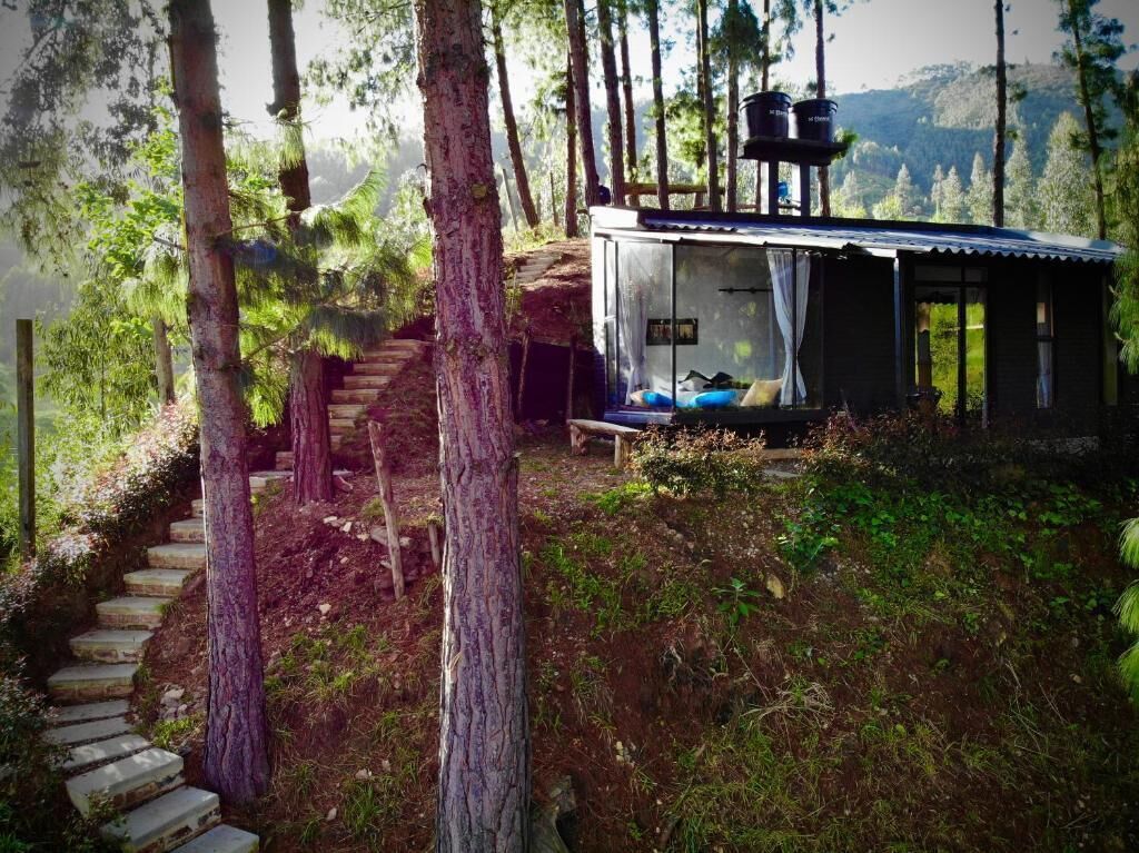 Eine Hütte mit einem Bett, einem kleinen Tisch und einem Fenster mit Blick auf ein bewaldetes Gebiet.