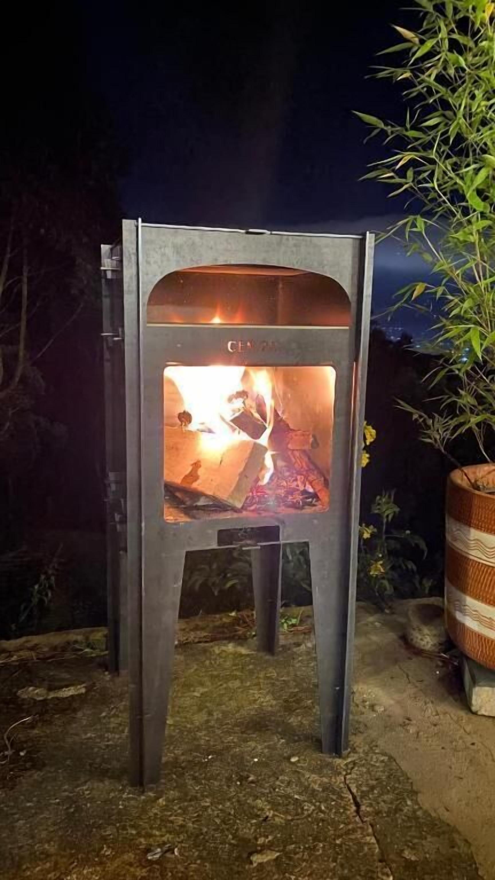 A metal outdoor grill with a fire inside, surrounded by a dark night setting.