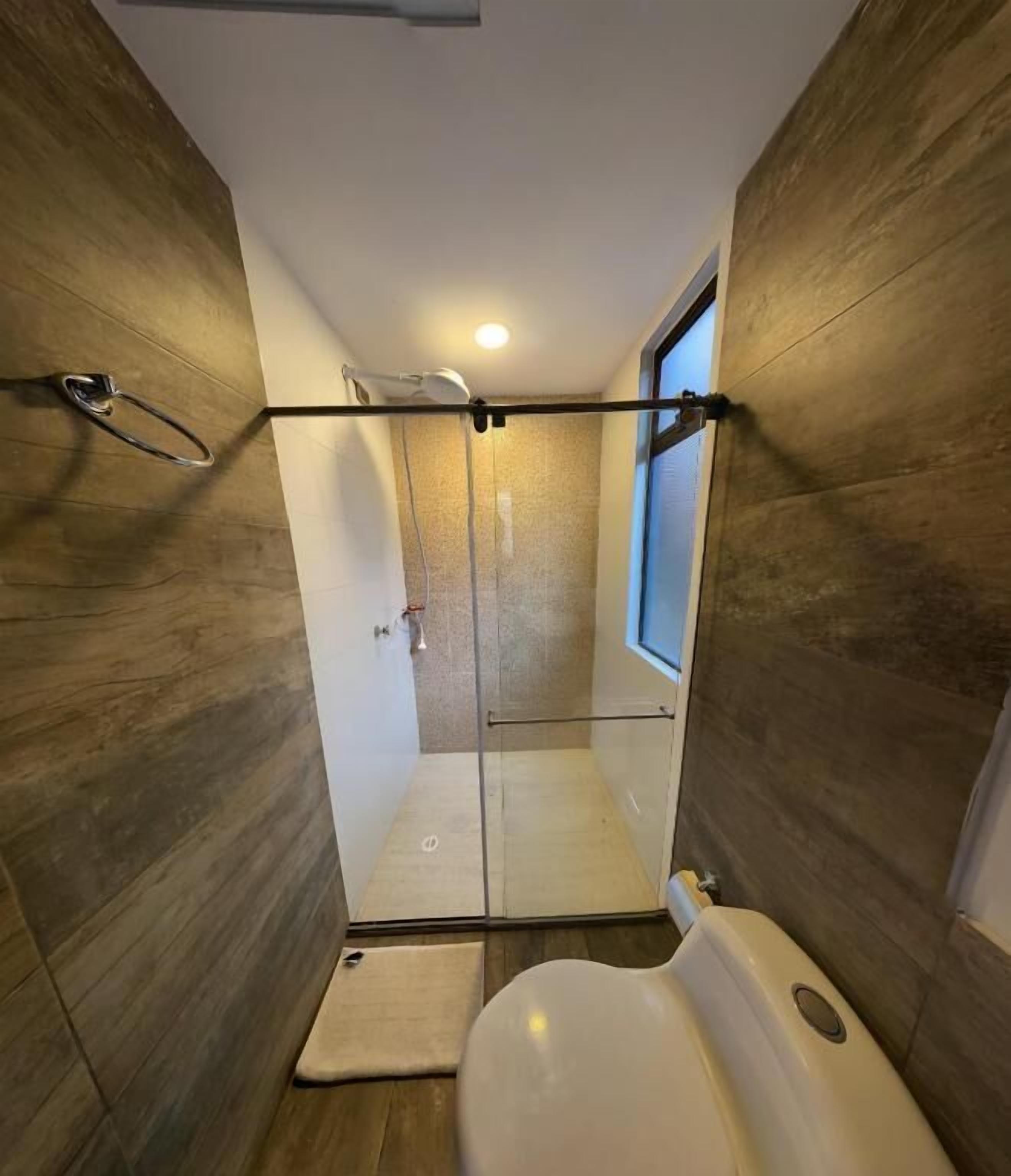 A compact bathroom with a shower, toilet, and a small window.