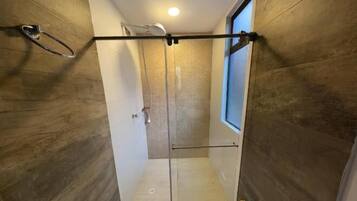 A compact bathroom with a shower, toilet, and a small window.