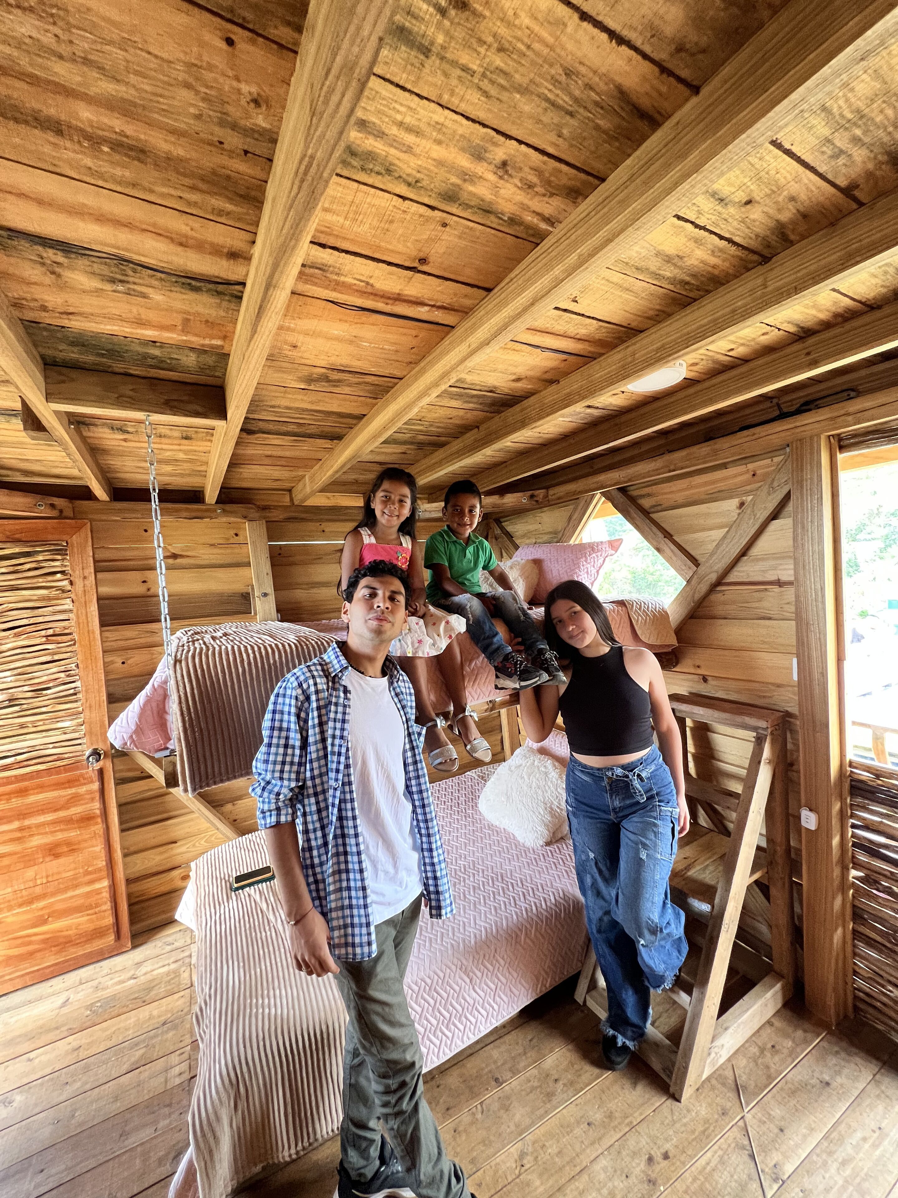 A rustic wooden cabin interior with a loft bed, a hanging hammock, and a wooden ceiling.