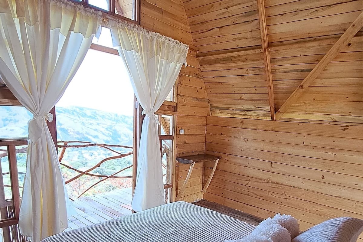 Ein Schlafzimmer einer Holzhütte mit Bett, Vorhängen und Blick ins Freie.