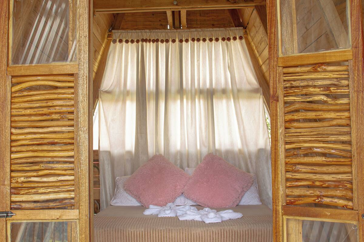 Eine Holzhütte mit Bett, Vorhängen und einem Fenster.