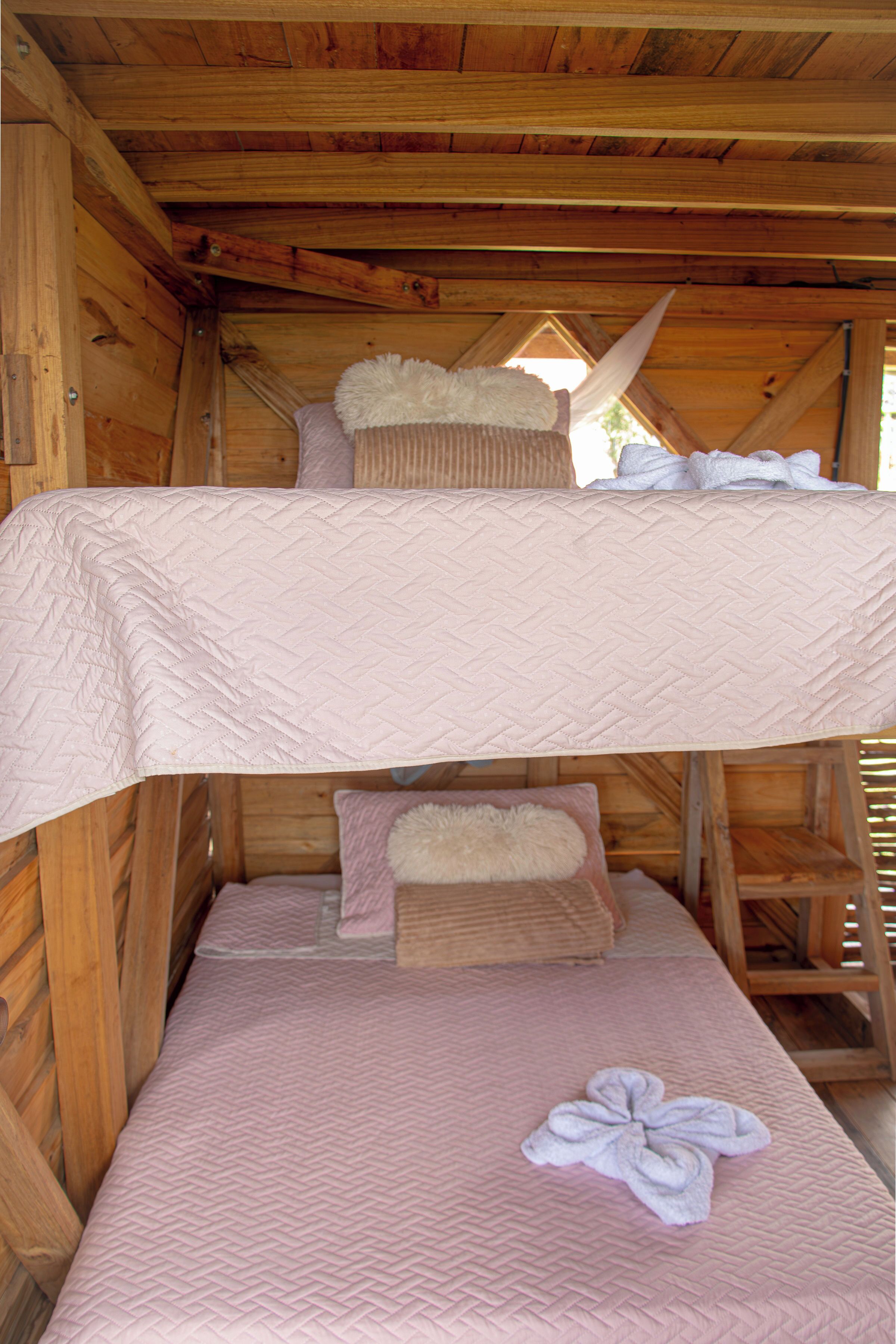 A bunk bed with a pink quilted mattress and a white fluffy pillow.