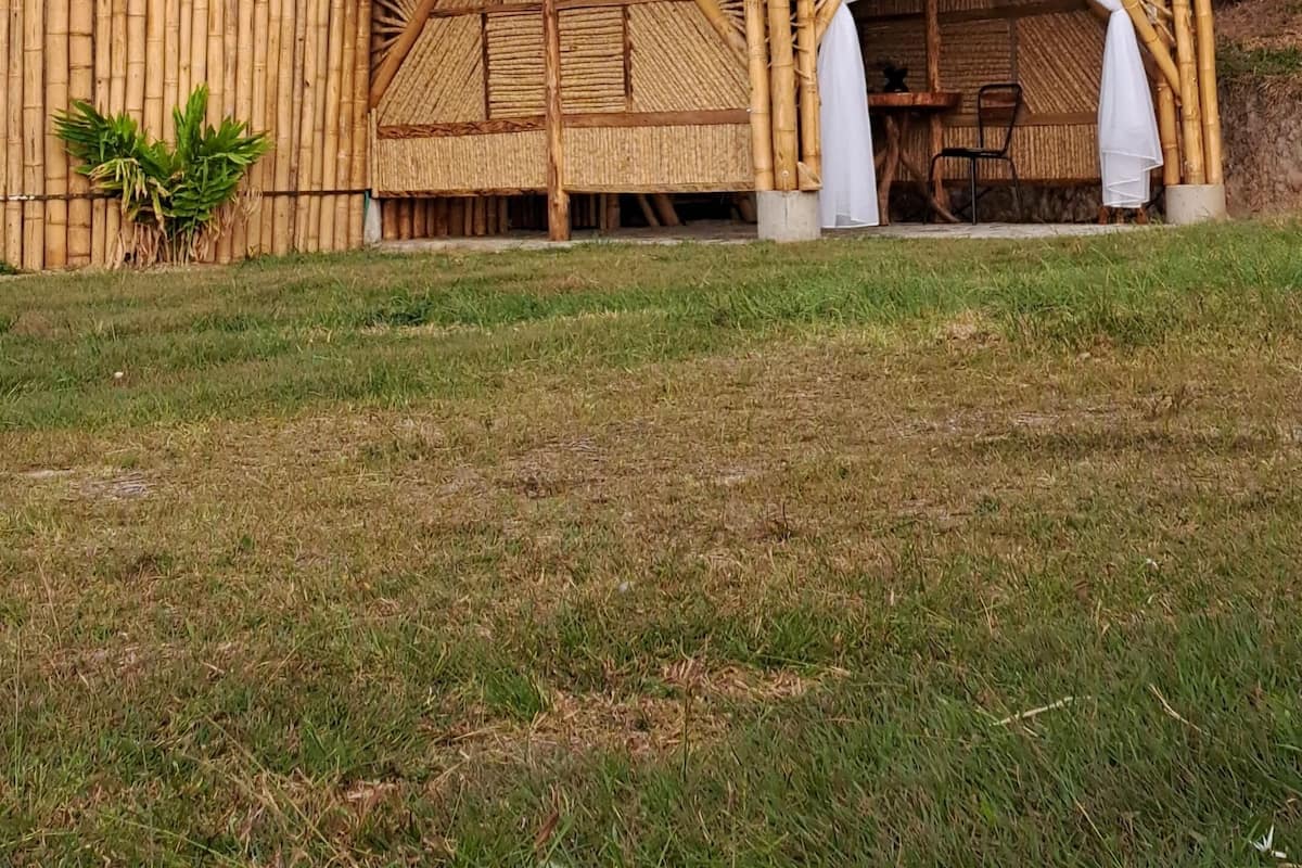 Eine rustikale Holzhütte mit rotem Dach, einem großen Fenster und einem Bambuszaun.