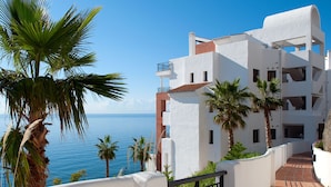 A coastal building with white walls and a red-tiled roof, featuring balconies and a paved walkway. - Sea Front by Interhome (Torrox Costa)