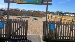 Señal de madera para Crazy Golf ASIS, con un área de juegos con arena al fondo.