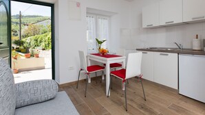 Een moderne keuken met witte kasten, een eethoek met een witte tafel en rode stoelen, en uitzicht op groen door een groot raam.