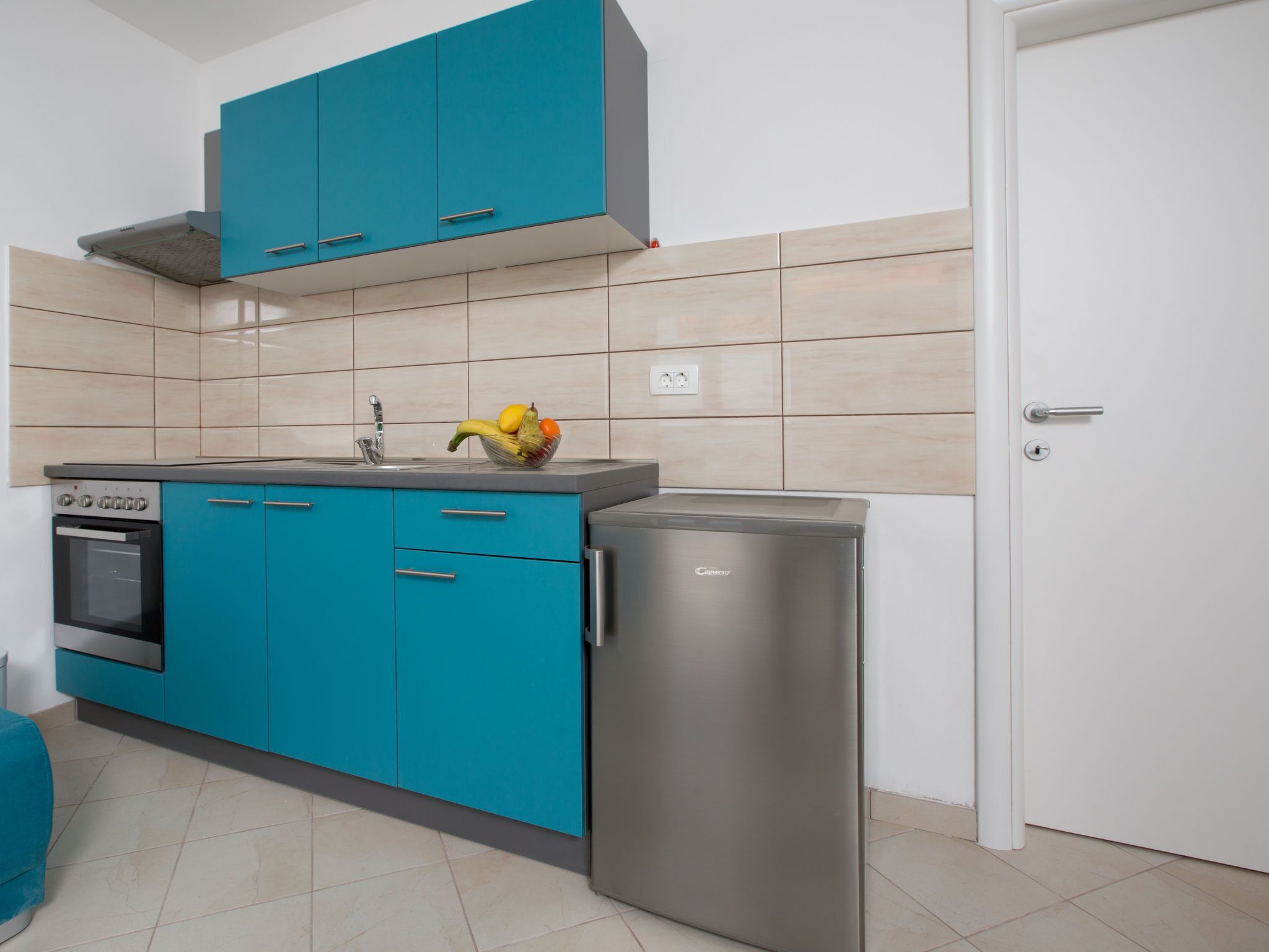 Une cuisine avec des armoires de couleur turquoise, un réfrigérateur en acier inoxydable et un four encastré.
