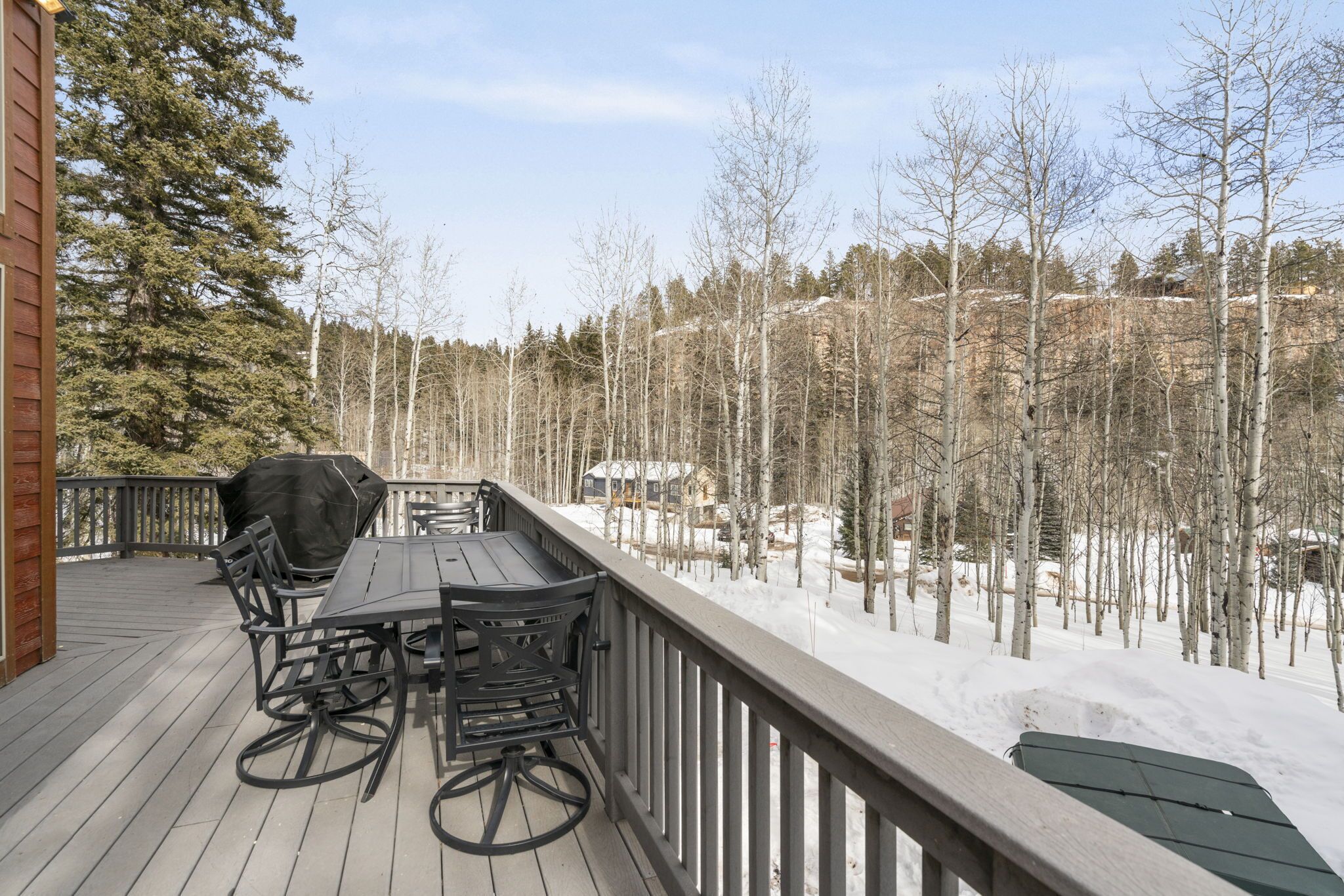 A wooden deck with a table and chairs, overlooking a snowy forest.