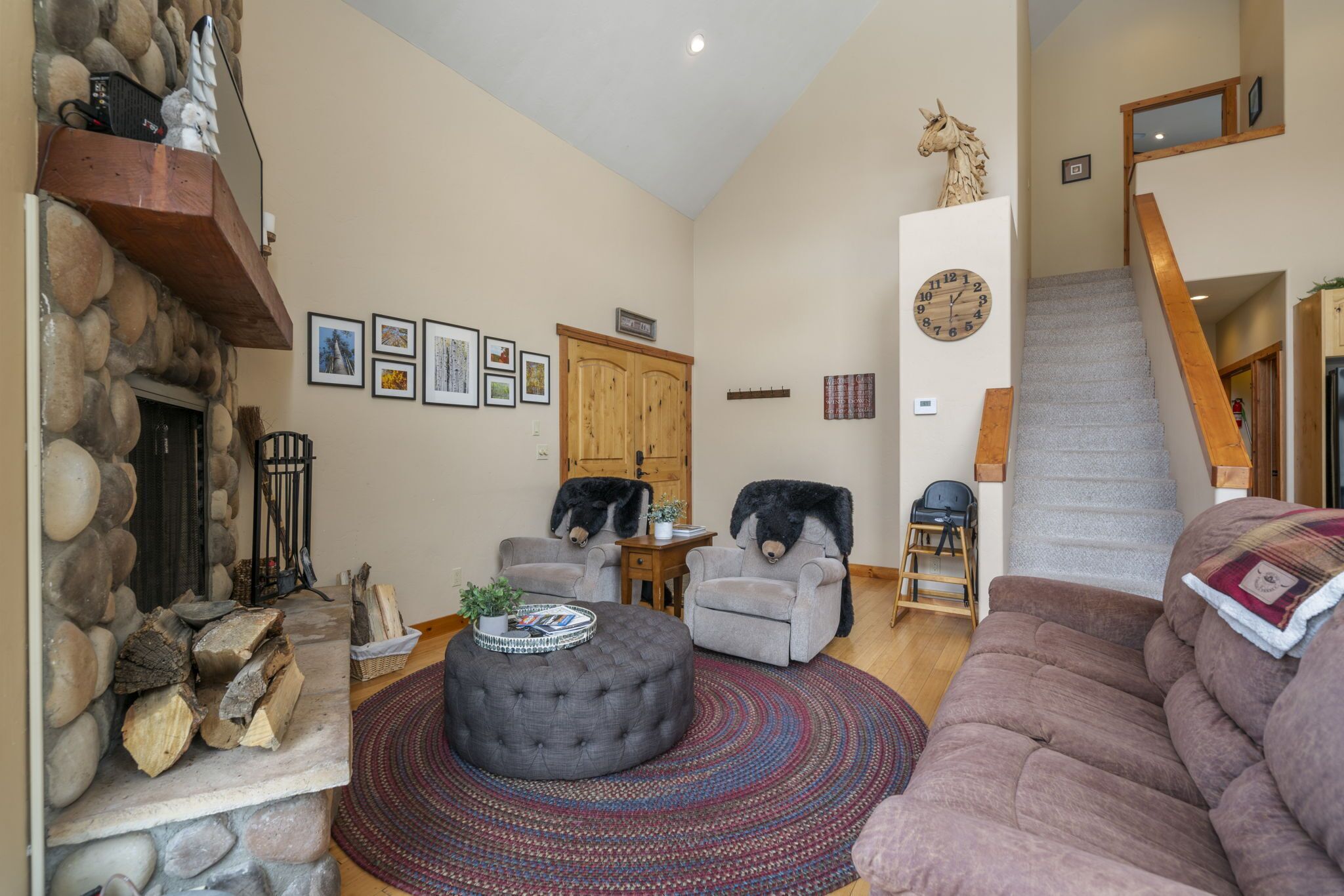 Un salon chaleureux avec une cheminée en pierre, des sièges confortables et un escalier menant à un autre niveau.