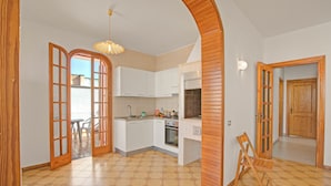 Een keuken met witte kastjes, een fornuis en een eethoek met een tafel en stoelen.