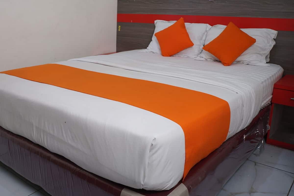 A bed with a white and orange bedspread, two orange pillows, and a wooden headboard.