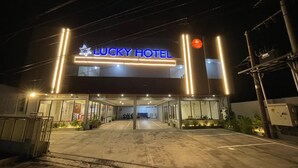 The exterior of the Lucky Hotel with a prominent illuminated sign, a gated entrance, and a parking area.