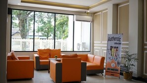 A modern hotel lobby with orange seating, large windows, and a banner advertising coffee and bakery services.