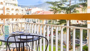 Ein Balkon mit Tisch und Stühlen, der auf eine Straße mit Gebäuden und Bäumen blickt.