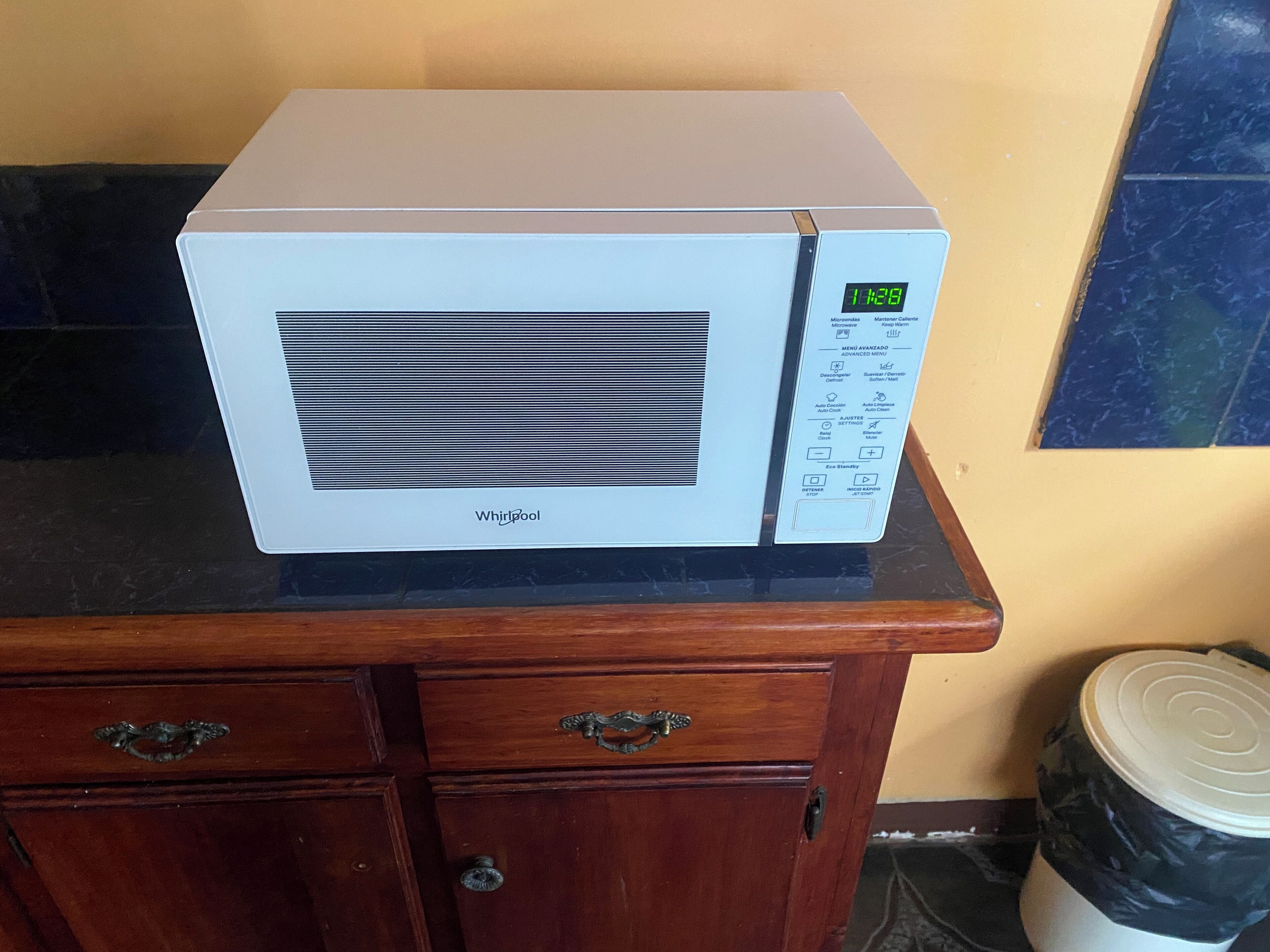 Un four à micro-ondes Whirlpool blanc, posé sur un meuble en bois et doté d’un écran numérique.