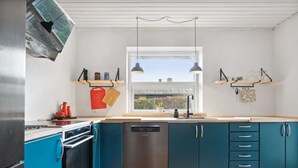 A modern kitchen with teal cabinets, stainless steel appliances, and pendant lighting.