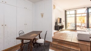 A dining area with a wooden table and chairs, a TV mounted on the wall, and a view of an outdoor patio with chairs and a table. - Santa Cecilia View by Interhome (Rome: Historical City Center)