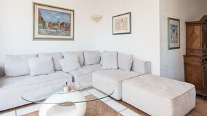 A living room with a light-colored sectional sofa, a glass coffee table, and a wooden cabinet. - Santa Cecilia View by Interhome (Rome: Historical City Center)