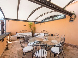 An outdoor patio with a round glass table surrounded by metal chairs, a sofa, and a small table with chairs.