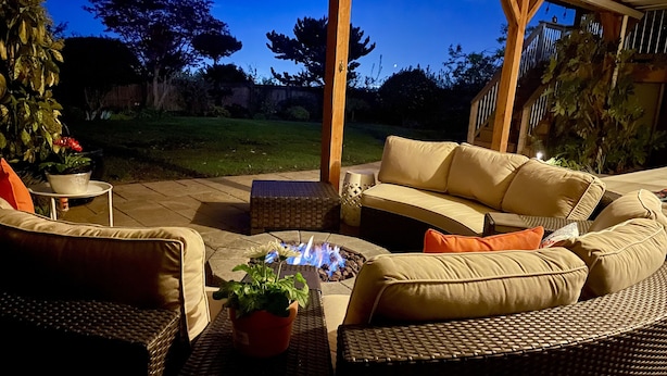 Ein Außenbereich mit Terrassenausstattung, Korbmöbeln, einem Feuerkorb und Blick auf den Garten.
