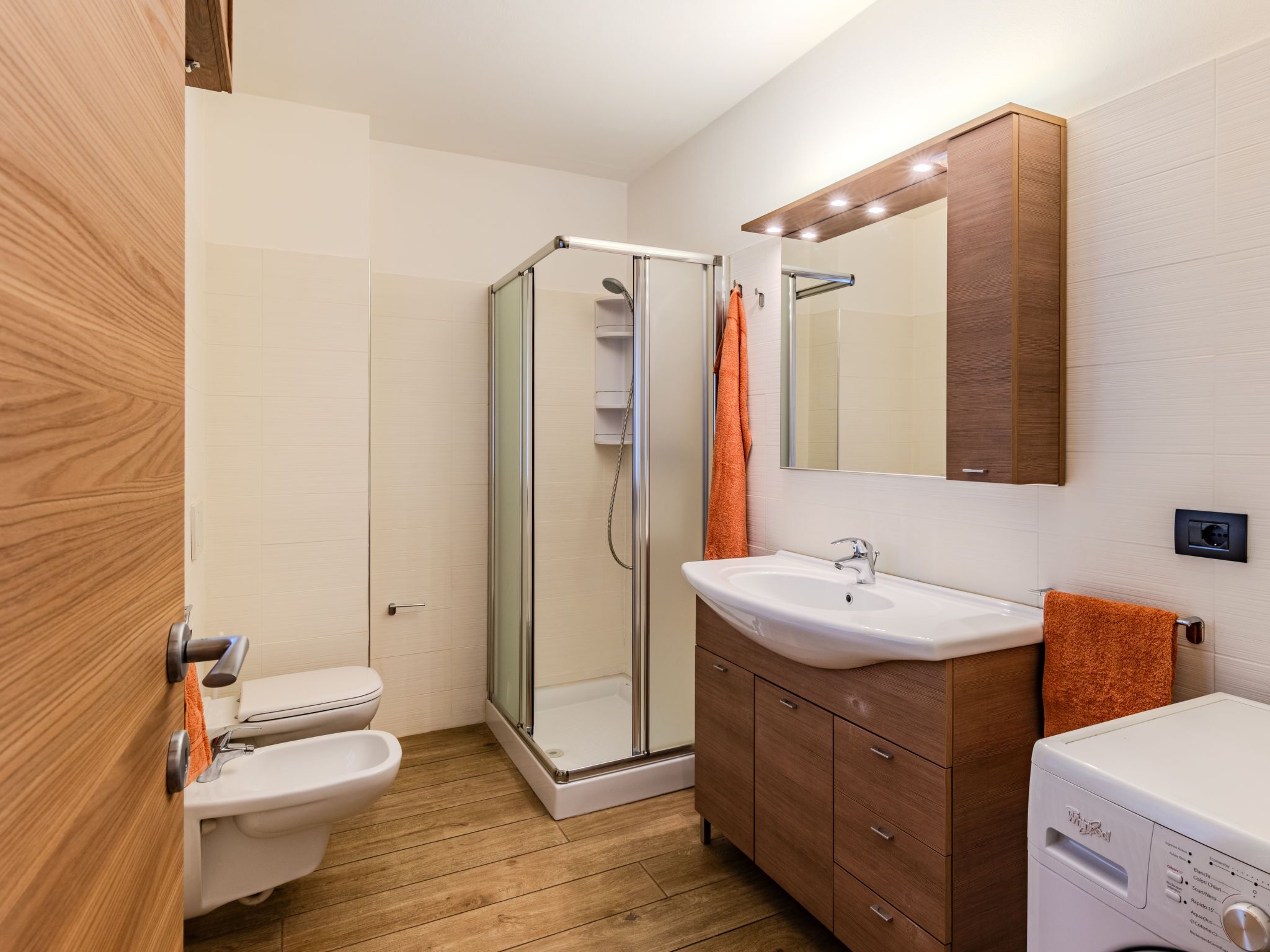 A modern bathroom with a glass-enclosed shower, a white sink, a wooden vanity, and a toilet.