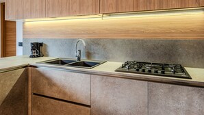 A modern kitchen with wooden cabinets, a stainless steel sink, a gas stove, and a coffee maker. - Santa Croce View by Interhome (Valtellina)