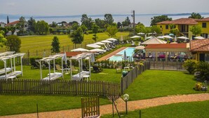A pool area with lounge chairs and umbrellas, surrounded by a wooden fence and a view of a lake.