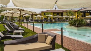 A poolside area with lounge chairs and umbrellas, a pool, and a building with yellow walls.