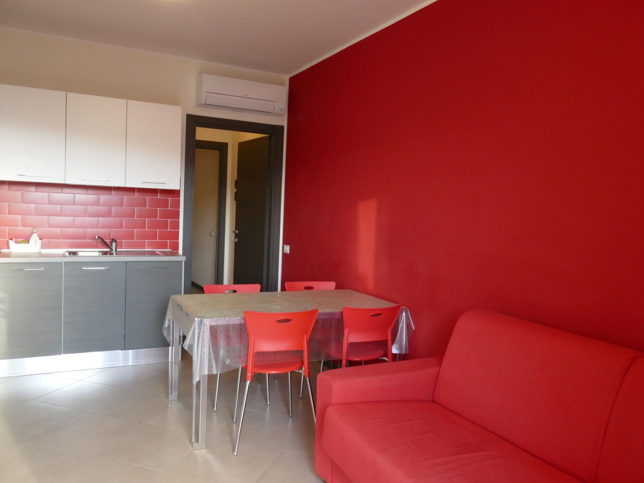 A compact living space with a kitchenette, a dining area with a table and chairs, and a red sofa.