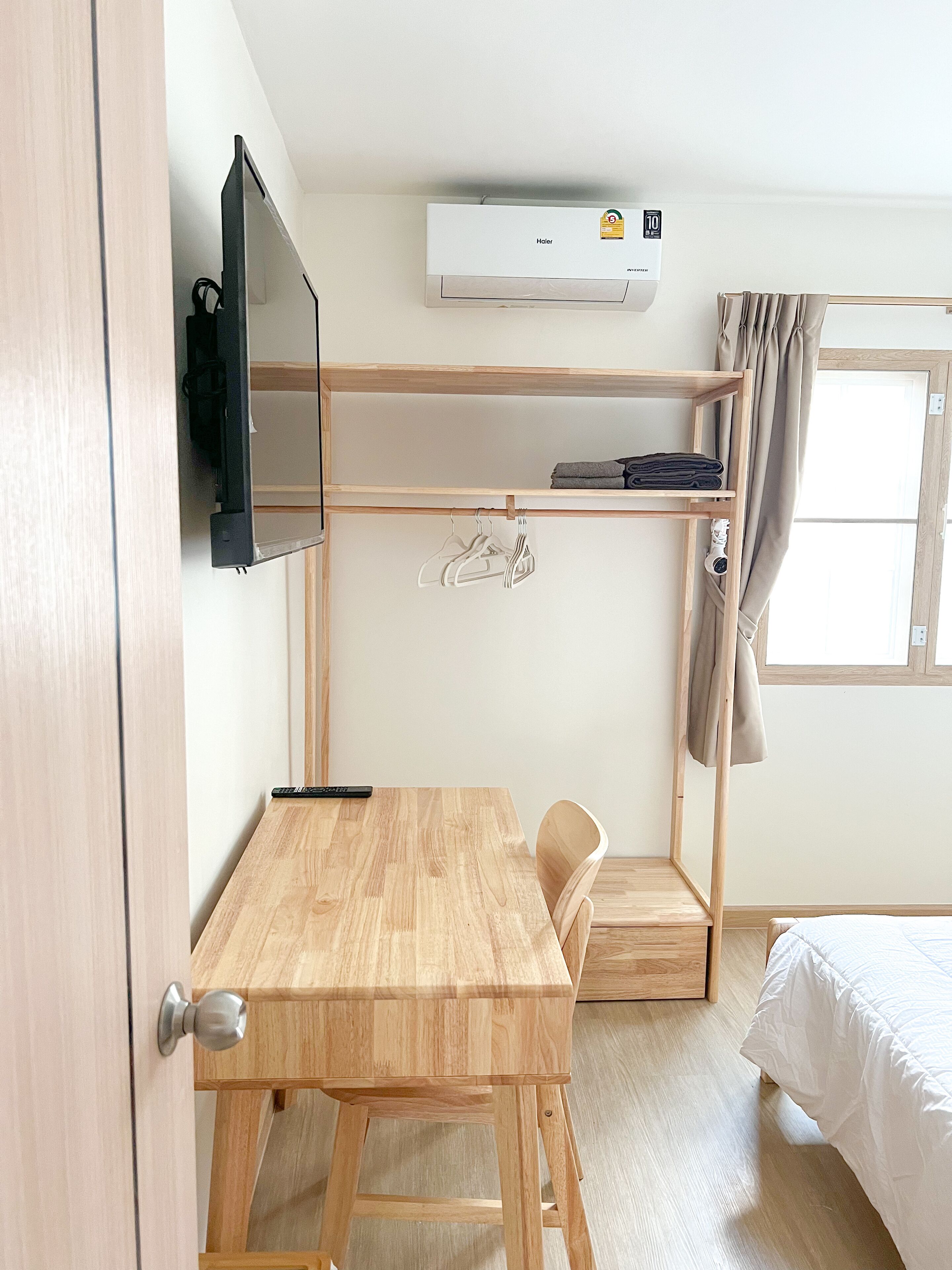Una habitación compacta con un escritorio de madera, una cama, un televisor instalado en la pared y aire acondicionado en el techo.