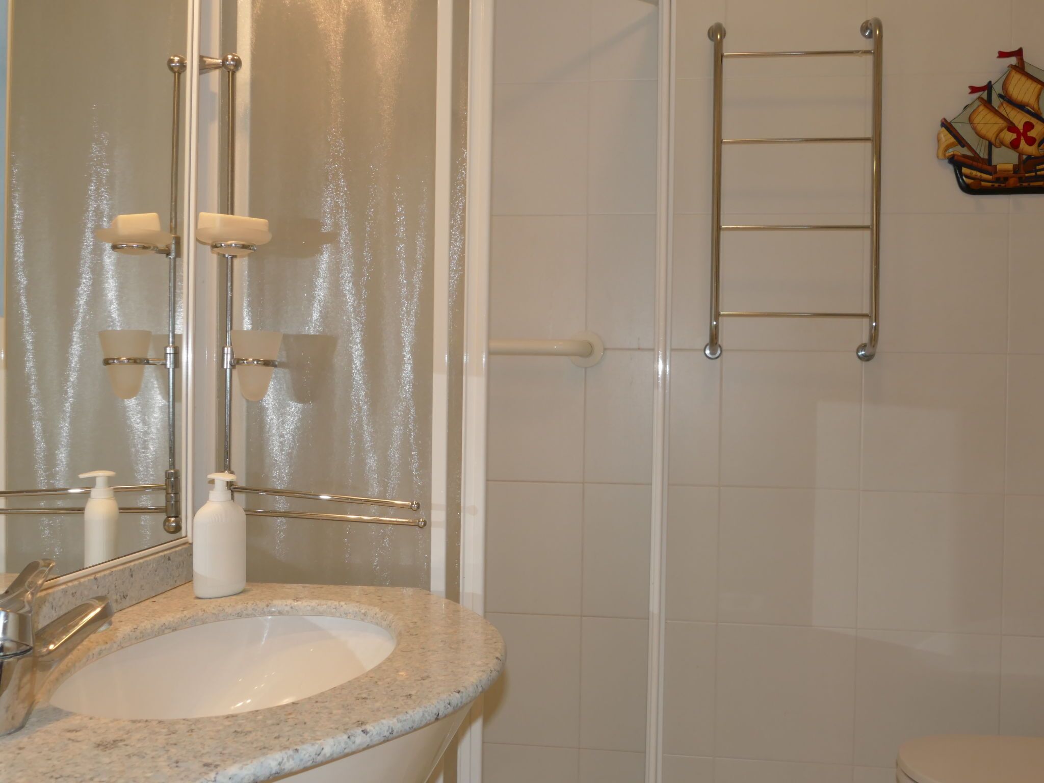A bathroom with a granite sink, a mirror, a towel rack, and a shower area.