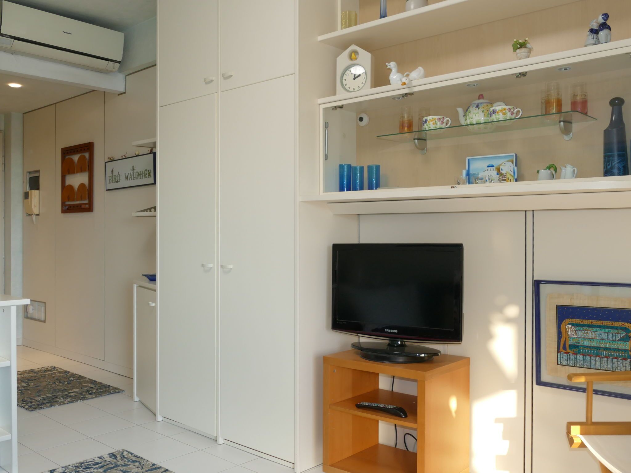 Un soggiorno moderno con una TV a schermo piatto su un mobile in legno, un armadio bianco e uno scaffale con oggetti decorativi.