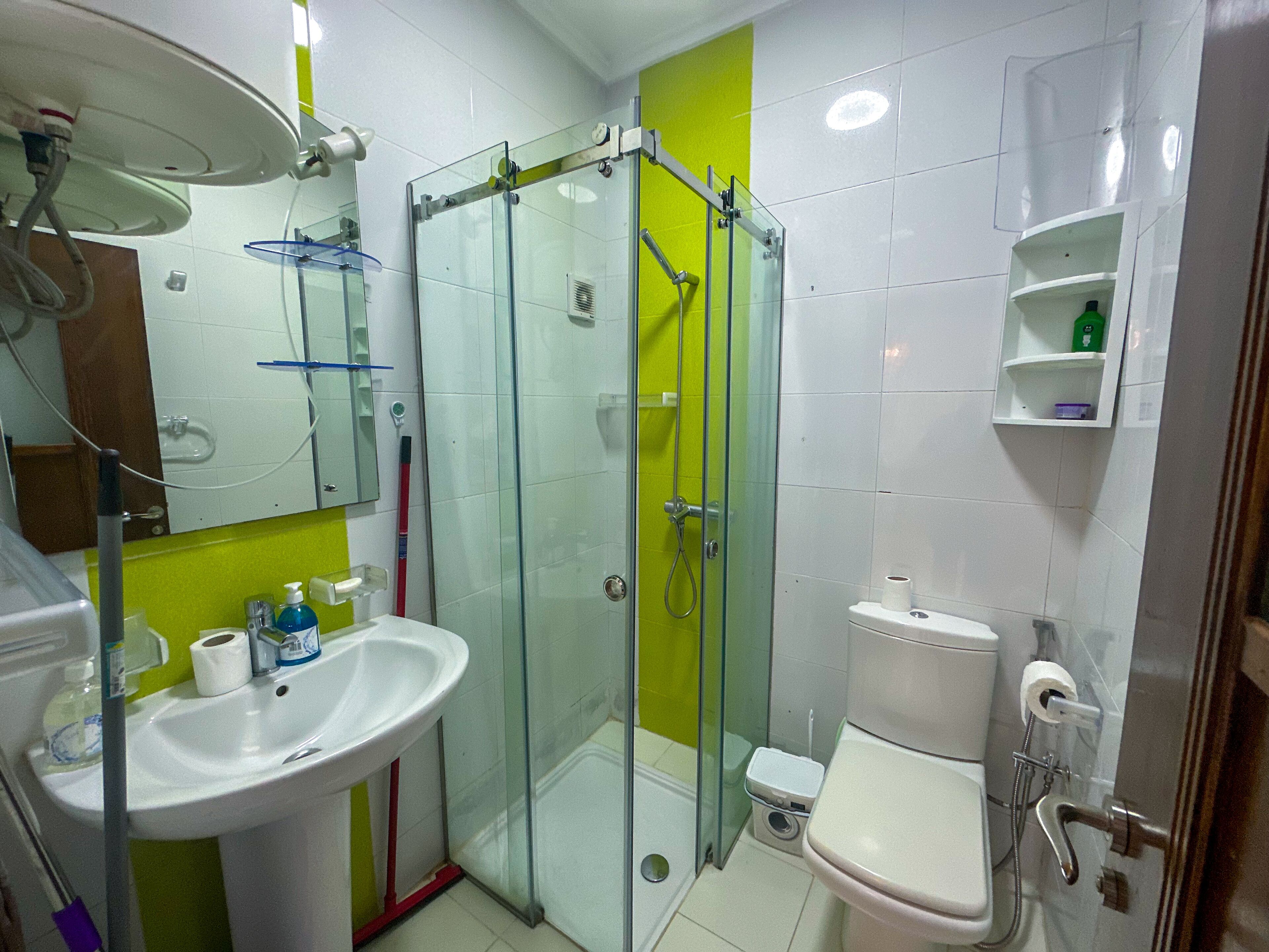 Een badkamer met een douche met glazen wand, een wit wastafelmeubel, een toilet en een spiegel boven het wastafelmeubel.