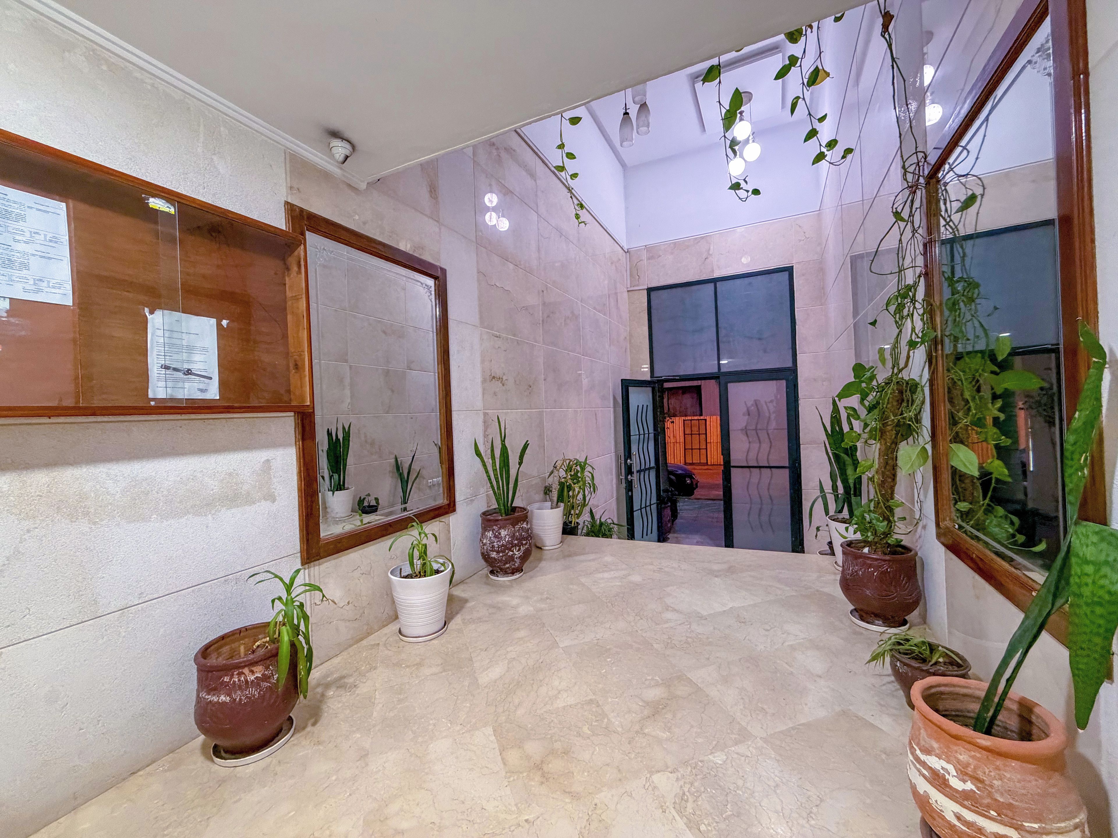 A lobby with a tiled floor, potted plants, a reception desk, and a door leading to another room.