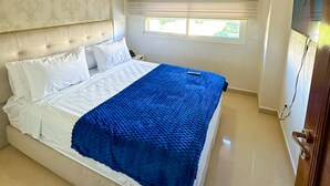 A bedroom with a bed, a window with blinds, a television on the wall, and a ceiling light fixture. - Luxury & Clean close to the Sea (Tangier)
