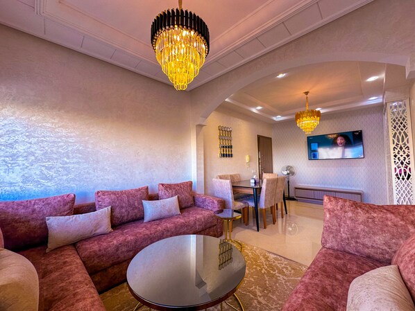 A modern living room with a plush pink sofa set, a round coffee table, and a chandelier.