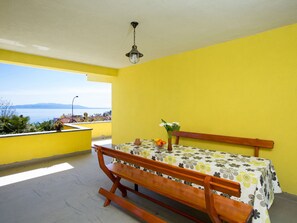 Una stanza con una parete gialla, una panca di legno, un tavolo con tovaglia floreale e vista sul mare.
